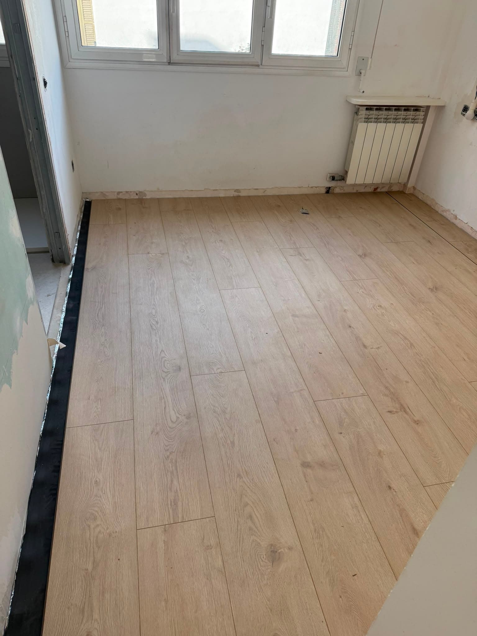 Habitación con la tarima de roble claro ya instalada y la junta de dilatación perimetral a la vista