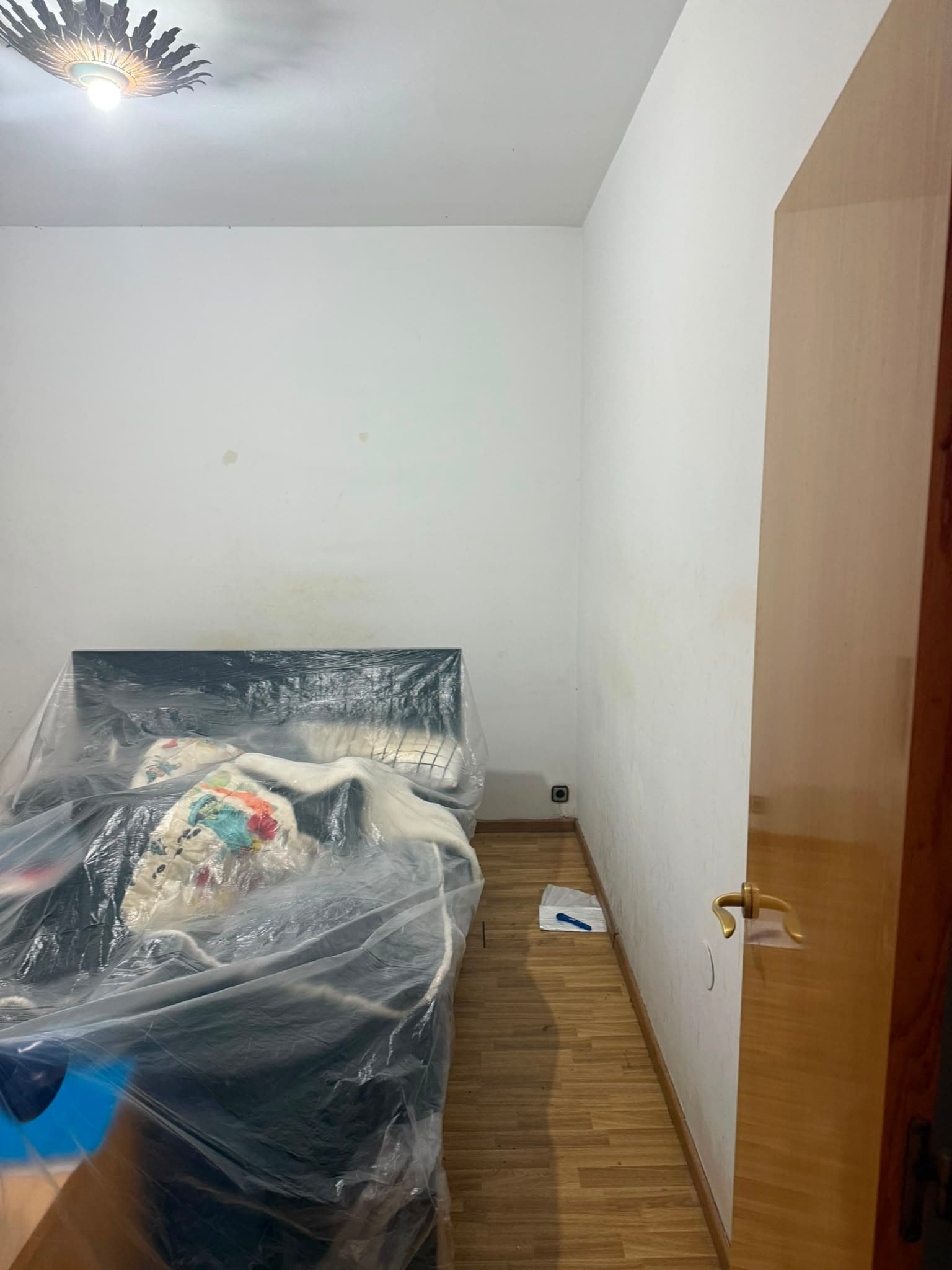 Dormitorio con las paredes manchadas y los muebles cubiertos con plástico antes de pintar