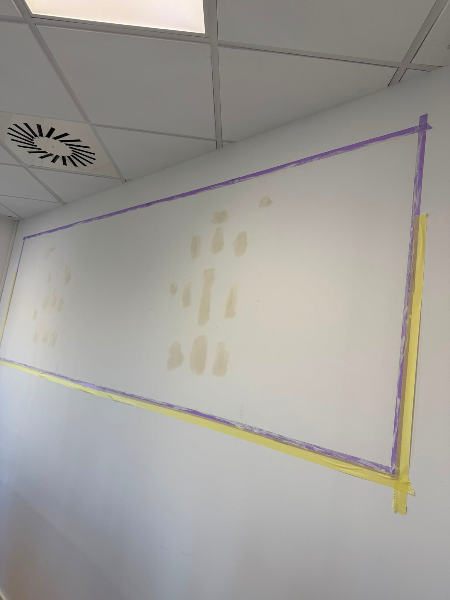 Pared de oficina con parcheos de masilla y cinta de enmascarar antes de pintarla