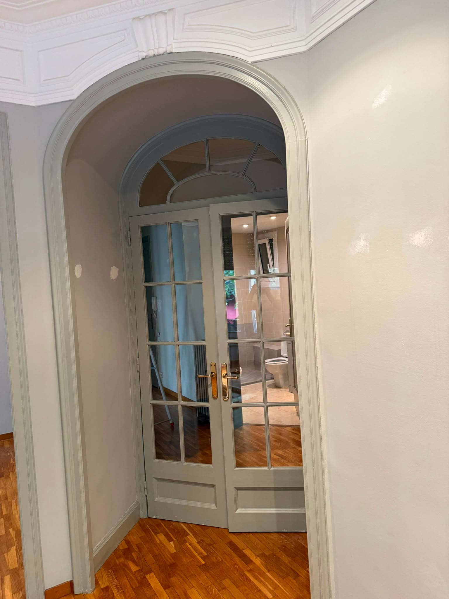 Arco y puertas acristaladas pintadas en verde grisáceo antes del lacado, en un piso clásico de Barcelona