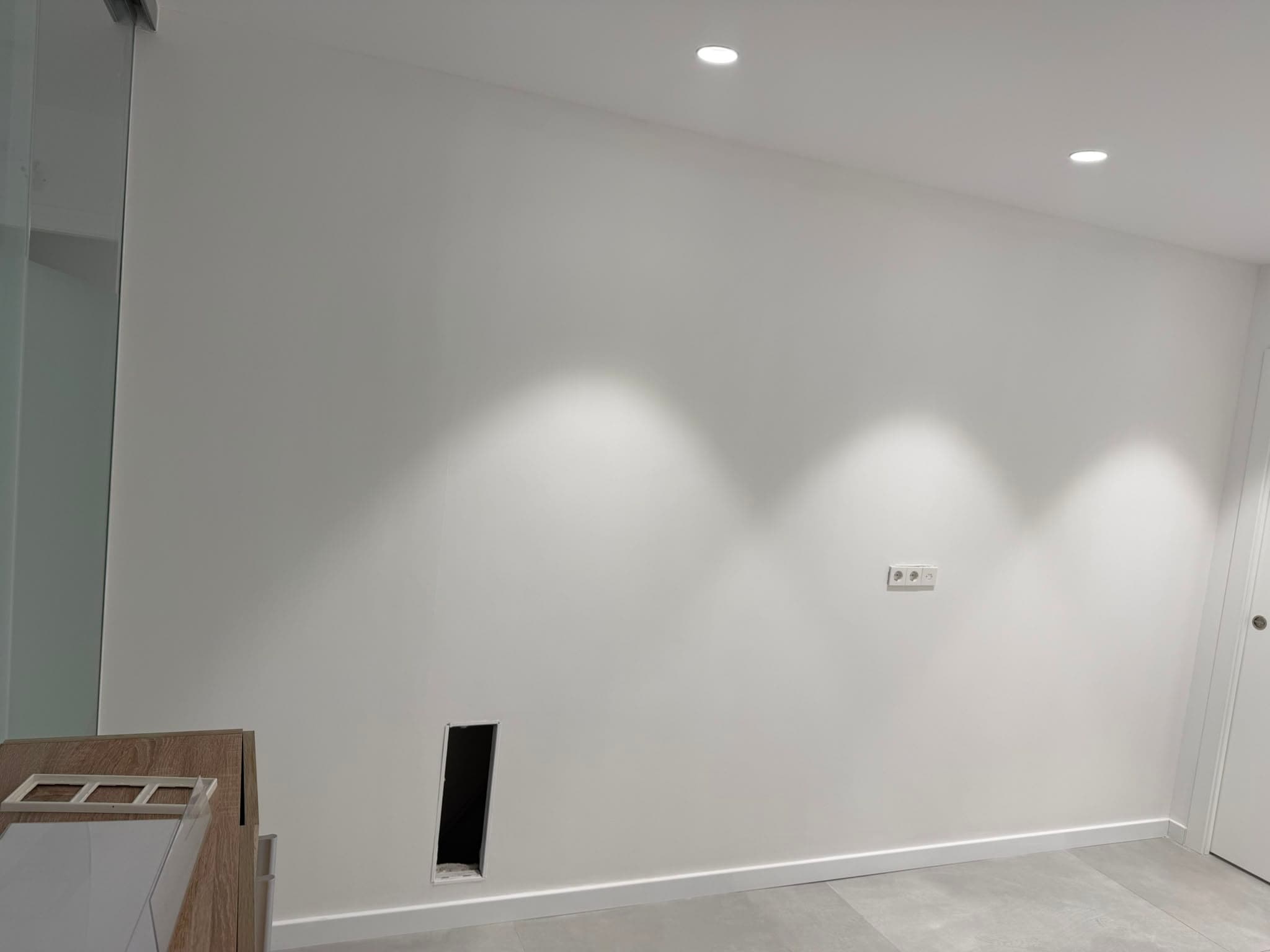 La misma pared uniforme y pintada en blanco, iluminada por focos empotrados